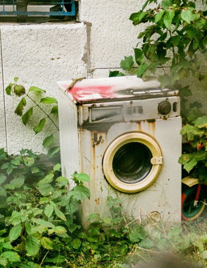 Defekte Waschmaschine Eine alte Waschmaschine steht draußen vor einer Hauswand, zugewachsen von Pflanzen.